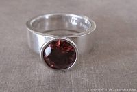 Front view of sterling silver ring with a bezel-set faceted deep red stone showing size and clarity of stone and band width.