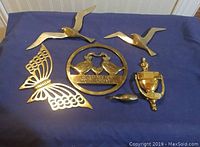 Full lot of five vintage brass items arranged on blue cloth: two flying birds, butterfly, Country Welcome plaque, and door knocker.