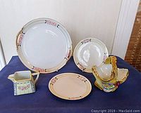 Full lot including floral basket, creamer, and three plates with hand-painted floral and geometric patterns.