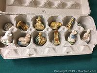Set of 12 ceramic tea figurines placed inside cardboard egg carton, showing variety of animals and people.