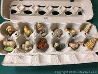 Top-view image showing 12 small tea figurines placed inside an egg carton with spaces, each figurine fitting into an individual slot.