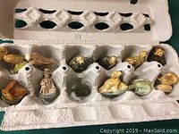 Photo of 12 small painted ceramic tea figurines in an egg carton, showing various animal shapes and a person in period attire.