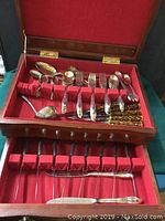 Full view of Rogers silverplate serving flatware arranged in wooden case with red velvet lining.