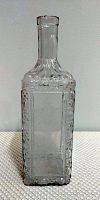 Clear glass decanter with rectangular body and textured sides placed against a neutral background.
