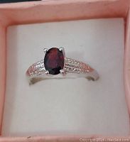Top and angled view of sterling silver ring with oval garnet gemstone in a textured setting inside a pink ring box.
