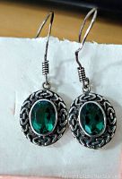 Pair of sterling silver drop earrings with oval green crystals and decorative silver framing, fishhook style backs shown.