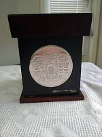 Front view of wooden storage box showing circular metal relief First Nations artwork and artist signature.