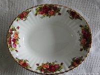 Oval vegetable serving dish with floral rose pattern and gold rim, on a white lace tablecloth.