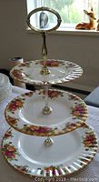 Photo of the entire three-tiered cake tray with floral plates, gold edges and a central gold handle