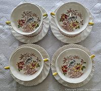 Top view of four double handled soup cups arranged on matching saucers, showing floral pattern inside cups and saucer detailing.