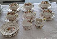 Teacups, saucers, napkin holders, cream jug, and sugar bowl arranged on cloth for full set view