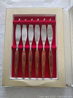 Set of six steak knives with teak wood handles in original presentation box.