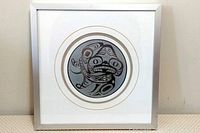 Front view of metal framed print of Haida Dogfish Drum artwork by Bill Reid, showing the circular black and gray dogfish design inside white double matting under glass.