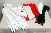 Photo showing all gloves and scarves laid out to display varying lengths and styles, including white gloves, red scarf, and black lace scarves
