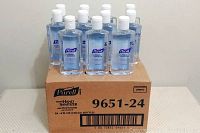 Thirty-five 4 oz Purell Advanced Hand Sanitizer bottles standing on and around a cardboard box labeled for 24 bottles.