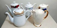 Group photo of all five tea pots together on beige surface, showing size and style variety