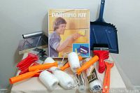 Painting lot items including paint kit box, paint rollers with orange handles, paint scraper, dustpan, red handle paint brushes, and metal masonry tool