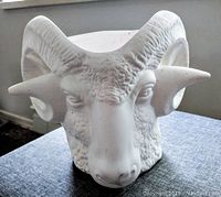 Front view of bisque ceramic planter shaped like a ram's head with horns, showing detailed facial features and hollow opening at the top.