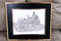 Framed black and white print showing a detailed drawing of Anne Hathaway's Cottage titled and signed by Anthony John, displayed on a couch.