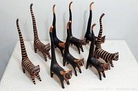 Wood carving lot with nine stylized cat sculptures in black and brown featuring striped and solid patterns, tall tails and detailed faces.