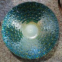 Top down view of the colorful decorative bowl showing the peacock feather pattern in blues, greens, and golds with glossy enamel finish.