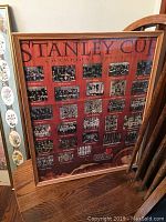 Framed Stanley Cup Champions poster showing multiple team photos and years on a reddish background with a wooden frame.
