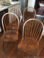 Four oak dining chairs with spindle back and medium brown finish shown in kitchen setting