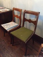 Pair of wooden side chairs side-by-side against wall, one with green upholstery, one seat has floral upholstery.