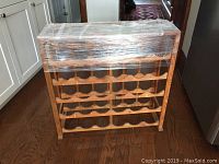 Front view of wooden wine rack wrapped in plastic film, showing multiple rows for bottle storage and glass top protection.