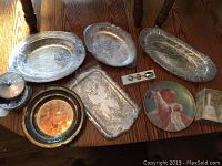 Photo showing six silver plate serving dishes and various decorative items on a wooden table.