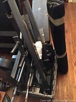Side view of metal weight bench frame parts stacked closely with a wrapped black exercise mat beside them.