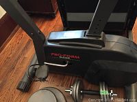 Side view of the Pro Form 940S exercise bike showing pedals, frame, and part of weights and dumbbell on floor.