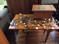 Small wooden table with broken leg with iron candle holder and glass tealight holders on top, hand painted foot stool nearby