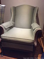 Front view of a wingback chair with green upholstery showing seat, backrest, and armrests.