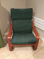 Front view of the green cushioned Ikea Poäng armchair with bentwood frame on tile floor near wall