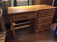 Front angle view of pine desk showing left large drawer and right side four smaller drawers with metal handles, natural pine finish, and slight surface wear.