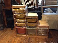 Full view of the step-shaped wooden storage unit with nine plastic bins wrapped in moving wrap.