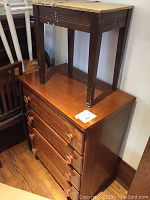 Chest of drawers with four wooden drawers, featuring round wooden pulls, with wooden stool on top showing wear and chipping on legs