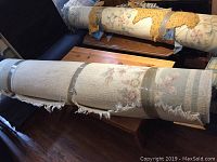 Rolled wool rug with visible floral pattern and pale green border, tan and cream colors, taped in two sections, showing frayed edges and some wear.
