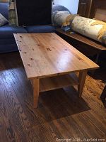 Full view of solid wood coffee table showing top surface and legs from an angle, against a background of sofa and rolled rug.