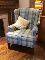 Full view of plaid wingback chair with throw cushion, showing overall design and color pattern.
