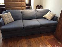 Full view of the three-seat sofa showing blue upholstery, fixed back cushions, and two throw pillows.