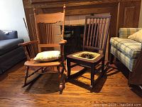 Two wooden rocking chairs side by side on hardwood floor in front of fireplace, larger chair with pillow on seat, smaller chair with damaged cane seat