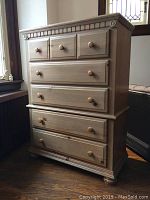 Front view of wooden highboy/tallboy dresser showing five drawers with round wooden knobs, natural wood finish, and decorative carved top edge.