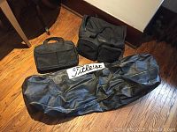 Photo showing the three black bags on wood floor: large Titleist golf bag, Calvin Klein duffle bag, and Bugatti laptop bag