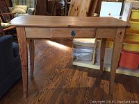 Full view of the small wooden sofa table showing its rectangular top, central drawer with keyhole decoration, and four tapered legs on hardwood floor.