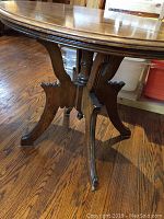 Close-up photo showing detailed carved wooden pedestal base and legs of the round table on wood floor.