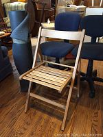 Wooden folding chair set up with two office chairs and rolled-up floor mat nearby.