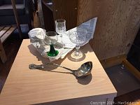 Three different glasses and one silver ladle spoon laid out on wooden surface with newspaper wrapping