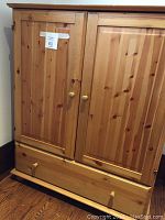 Front view of pine cabinet with two doors and bottom drawer, showing wood grain and knobs.